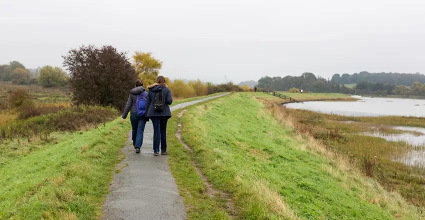 2 female friends enjoying a walk along a river path on a dull and rainy autumn day