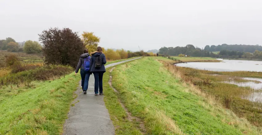 2 female friends enjoying a walk along a river path on a dull and rainy autumn day